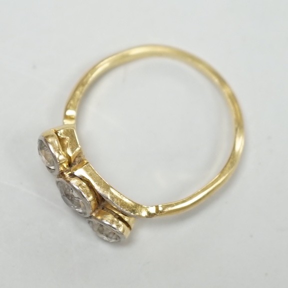 A yellow metal and three stone diamond set crossover ring, size N/O, gross weight 3.1 grams.